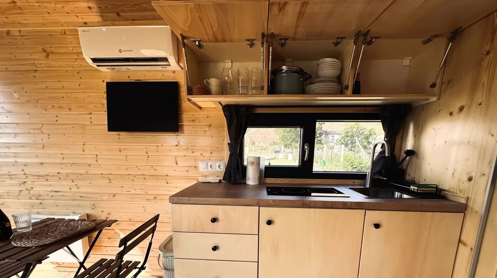 Cucina con piano cottura, lavello, pensili aperti e televisore a parete
